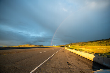 A rainbow shining beyond an empty countryside highway.   Merritt BC Canada
