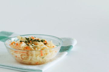 homemade sauerkraut with orange carrots with herbs in a glass plate on a white background. Pickled cabbage in glass bowl with textile on the table. copy space. vegetarian food.