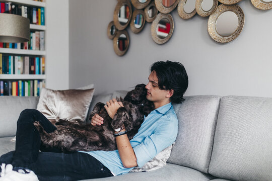 Young man cuddling the cocker spaniel dog on his lap on the couch at home