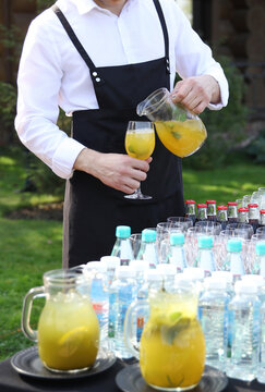 Catering. The waiter pours juice from a jug, lemonade in glass with hands. Summer, Sunny day. Banquet. Soft drink. Background image, copy space