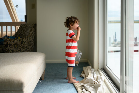 Young boy eating crackers while standing on curtains he's torn down