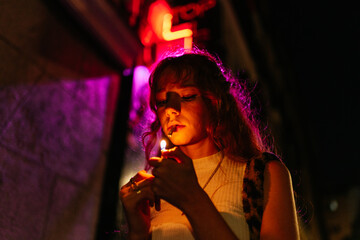 redhead woman lights a cigarette or a joint in the street at night