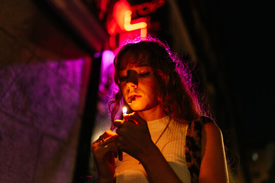 redhead woman lights a cigarette or a joint in the street at night
