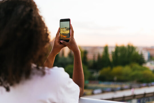 rear view of a curly hair woman taking a picture of sunset