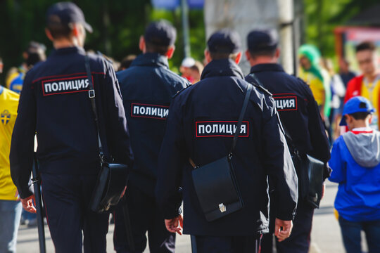 Russian police squad formation back view with "Police" emblem on uniform maintain public order after football game with football fans crowd in the background