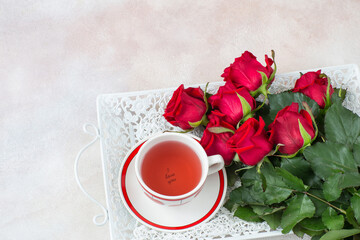 on a tray a bouquet of red roses and a cup of tea 