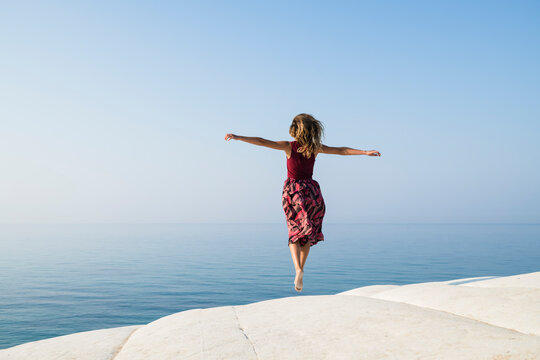 Young woman jumping on a white rock against deep blue sea