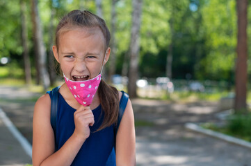 Portrait of a happy caucasian little girl taking off face mask outdoors. Finally, quarantine will end. Victory over the coronavirus.