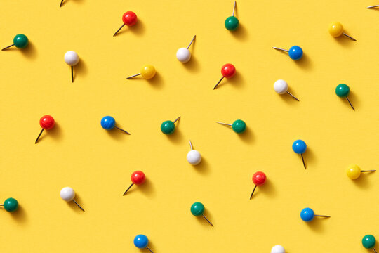 Office supplies pattern of multicolored pins on yellow.