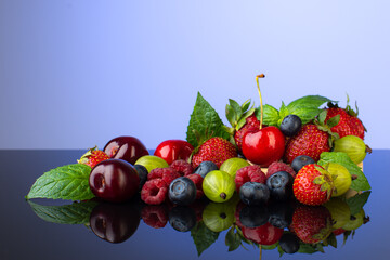 Summer berries on the table with reflection:strawberries,cherries,raspberries,goosberry and blueberry,with fresh minr leaves.
