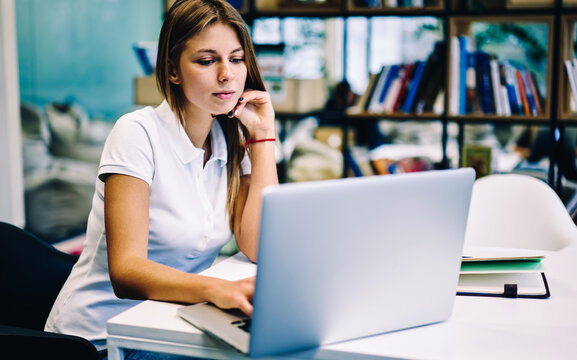 Concentrated female student watching training webinar online on laptop computer prepare for exams in library, smart hipster girl spending time on autodidact via e learning program courses via netbook