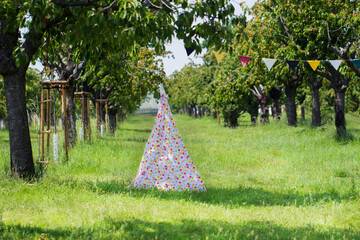 Children's tent wigwam white with colored circles in the Park and colored flags.The concept of a children's holiday in the open air on a Sunny summer day © Elena