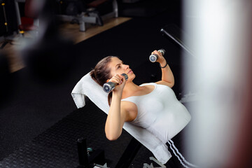 Young  and beautiful woman exercise in gym, she is doing incline bench press with dumbbells