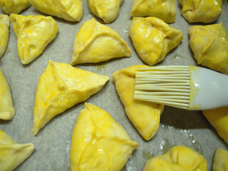 Homemade oiled pies are on a baking sheet on baking paper.