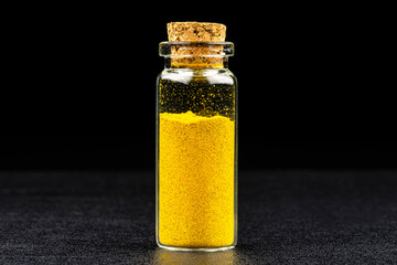 Macro shot of curries spice in a small glass bottle closed with a cork, isolated on a black background.