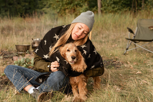 The blond girl in the hat and blanket with stars hugs her english cocker spaniel in the forest