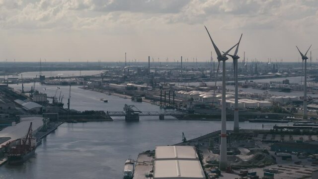 Aerial of the port of Antwerp depicting main canal  old industrial buildings in the foreground and petrochemical industry in the background. Wind turbines spinning on a sunny day with some minor cloud