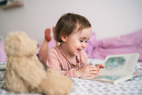 Adorable toddler girl lying on bed watching book
