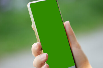 a woman's hand holds a modern smartphone on a green street background.close up.green screen for...