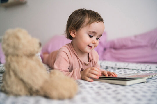 Adorable toddler girl lying on bed watching book