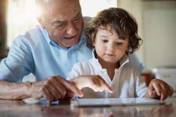 2 year old boy with his grandfather using a digital tablet