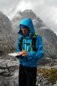 Trail runner using compass and a map on a rainy day close to gray limestone mountains