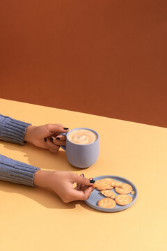 Holding warm coffee and eating cookies. Woman hands