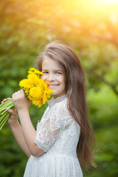 fashionable girl in a light dress poses and holds a large bouquet of yellow dandelions