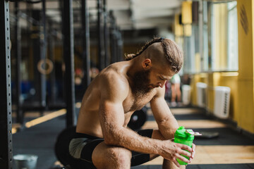 Strong and healthy man drinking water on a rowing machine, inside a crossfit gym.