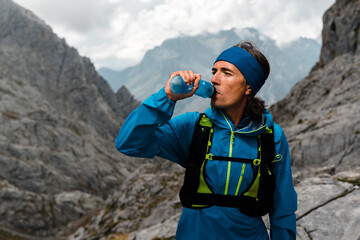 Trail runner drinking water on a rainy day close to gray limestone mountains