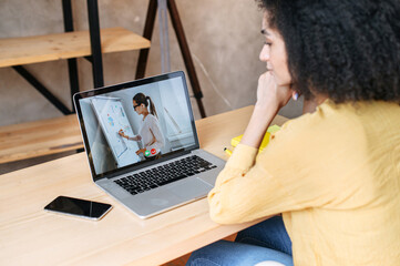 Webinars, lectures online. A biracial woman in office is watching online classes, female teacher on...