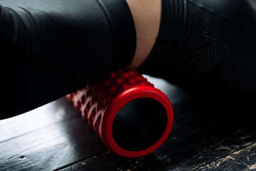 Close-up of a girls lower back under which lies a sports massage cylinder to strengthen fascia of the lumbar muscles of the back.