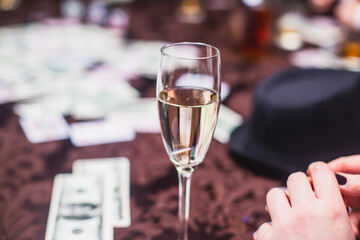View of poker table with pack of cards, tokens, alcohol drinks, dollar money and group of gambling rich wealthy people playing poker