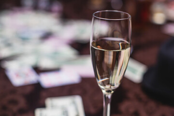 View of poker table with pack of cards, tokens, alcohol drinks, dollar money and group of gambling rich wealthy people playing poker