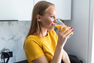 Attractive young woman holding a glass of orange juice while standing in the kitchen