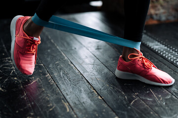 Closeup of legs of a girl in pink sneakers taking steps with rubber athletic tape at the ankles in the gym.