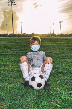Muddy young soccer boy sitting on field wearing virus mask