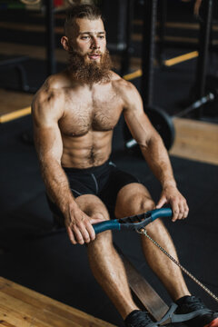 Strong and healthy man working out on a rowing machine, inside a crossfit gym.