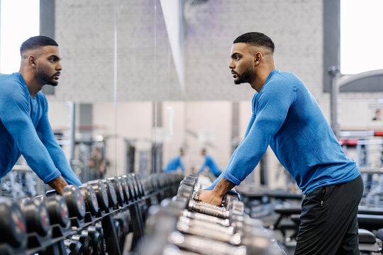Athletic man waiting and looking at himself in front of the mirror at the gym. - Powered by Adobe