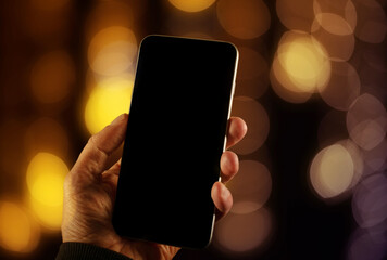 Close up view of a man using empty screen smartphone with background defocused warm colored lights