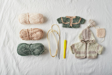Handmade knitted small sweaters and threads on light background.