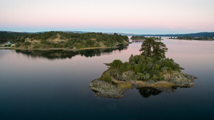 The lake at nightfall. Beautiful aerial view of an island, the lake, coastline, reflection in water and forest at nightfall. 