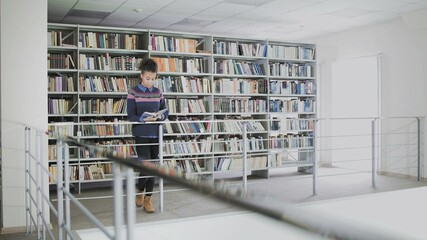 Young pretty african american woman is reading book whlie standing before the shelves in the library