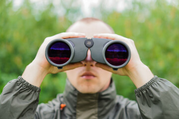 Fototapeta premium A young hunter in the forest looks into the binoculars. He is looking for wild animals.