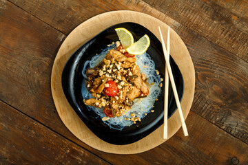 plate with funchose and chicken with vegetables in pad Thai sauce next to chopsticks on a stand.