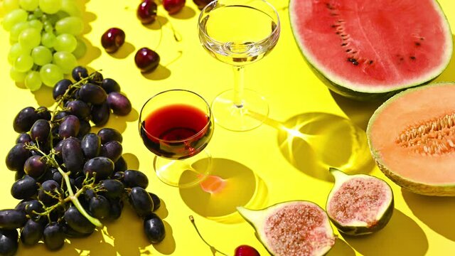 
Two glasses of red and white wine. A woman pours wine from a bottle. Grapes and other fruits on a yellow background. The concept of harvest and Italian winemaking. Stop motion.