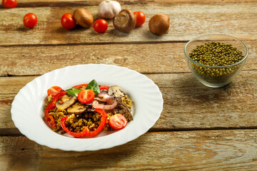On a wooden table is a white dish of boiled mung bean with mushrooms and vegetables. Ingredients nearby
