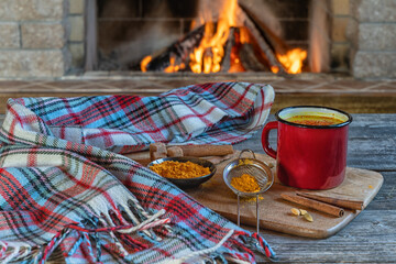 Golden latte milk in red mug with turmeric and spices before cozy fireplace. Healthy drink.