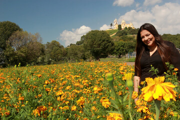 Obraz na płótnie Canvas Latin adult woman in field of yellow flowers, in the background pyramid and church of Cholula Puebla Mexico