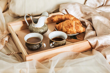 Two cups of coffee and croissants on a wooden tray in a silk bed. Romantic morning atmosphere, breakfast in bed. Home interior. Lifestyle.
